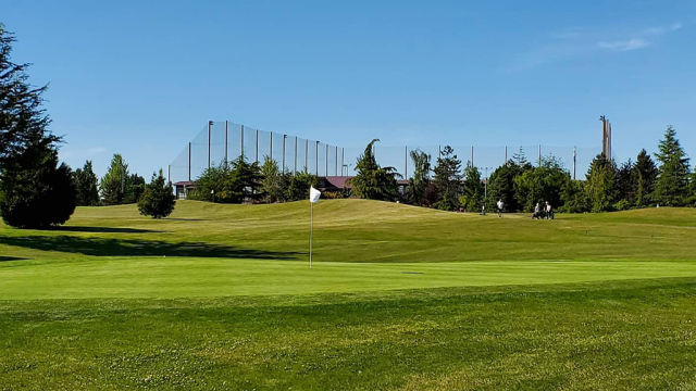 View of flag on golf course with driving range in distance