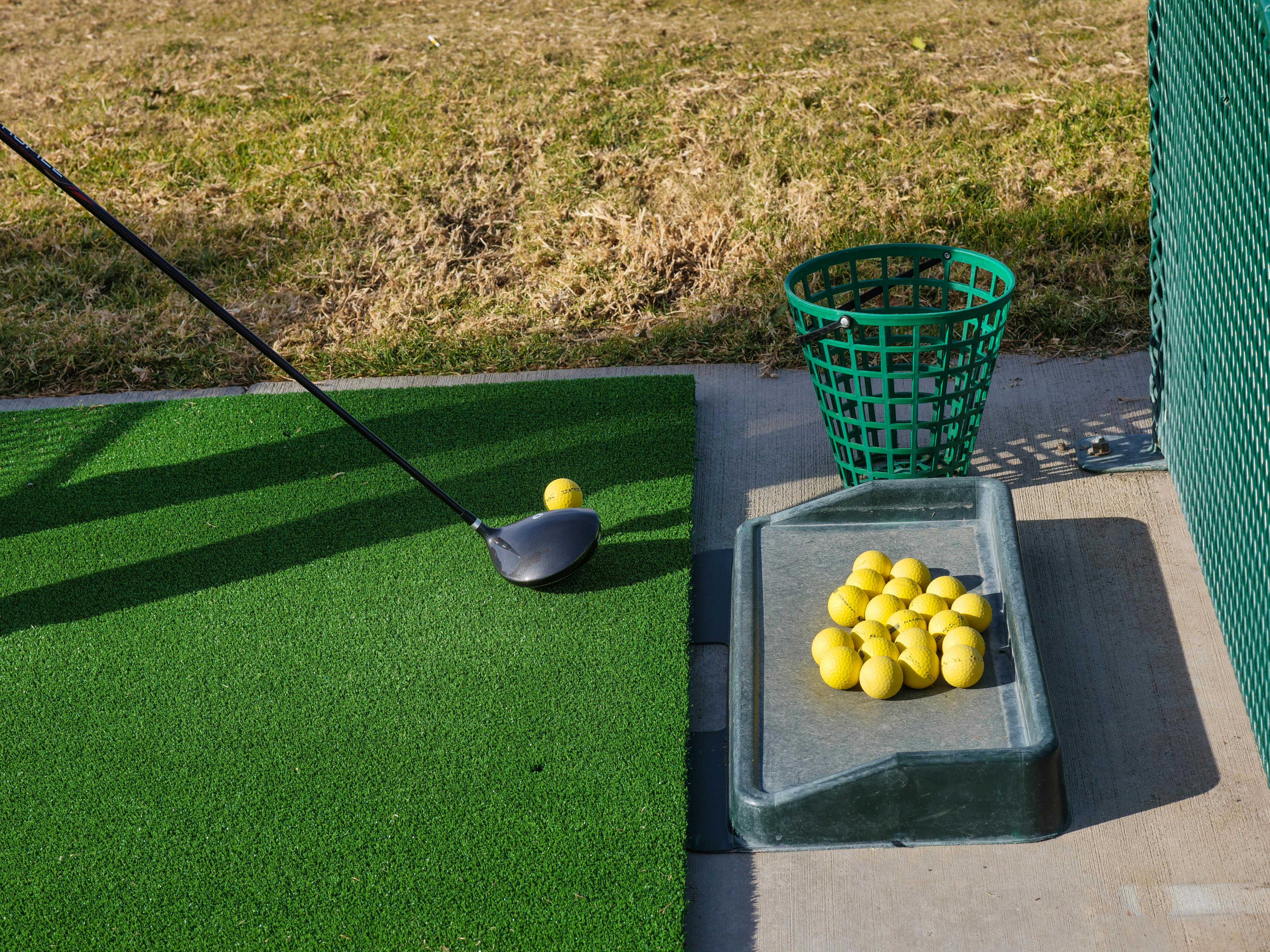 Range shot of club near ball adjacent to empty bucket of range balls by plane of all range balls